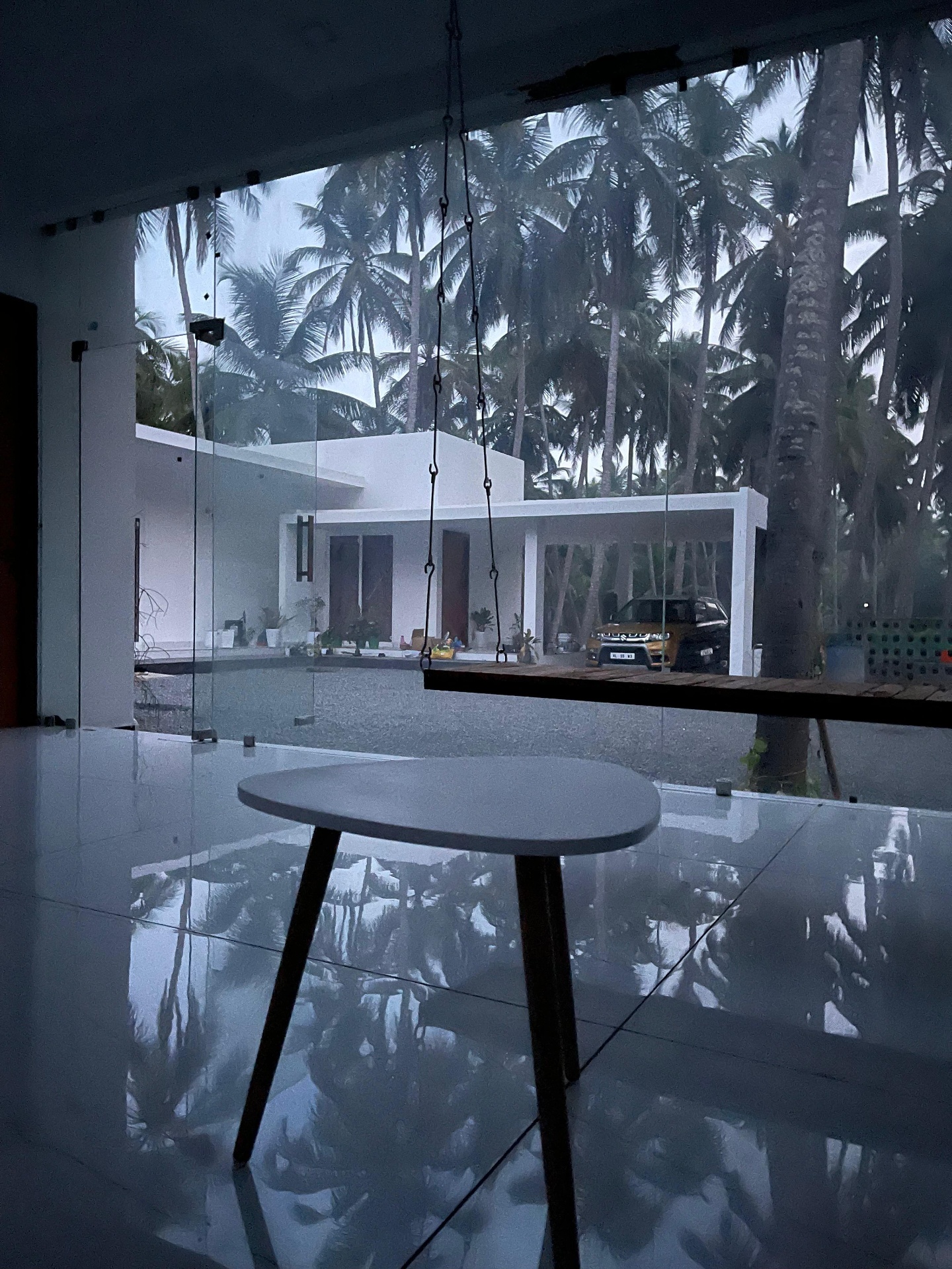 Glass-walled sit-out with side table overlooking landscaped courtyard and carport — iptnirman architecture