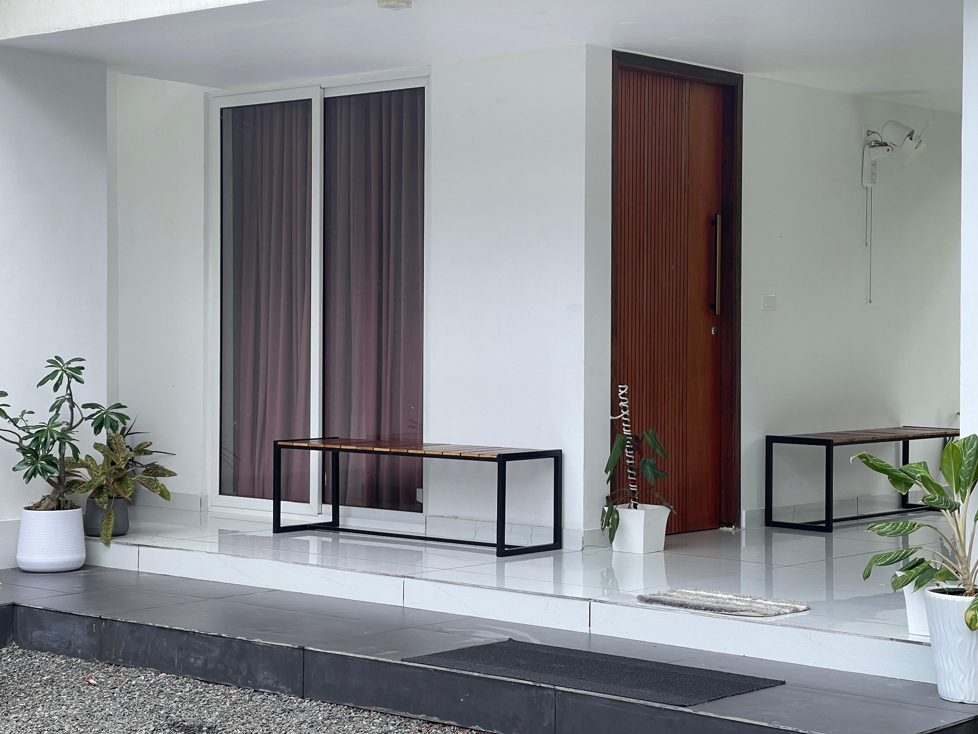 Contemporary villa entrance with teak pivot door, wooden bench and potted greenery — iptnirman turnkey residence