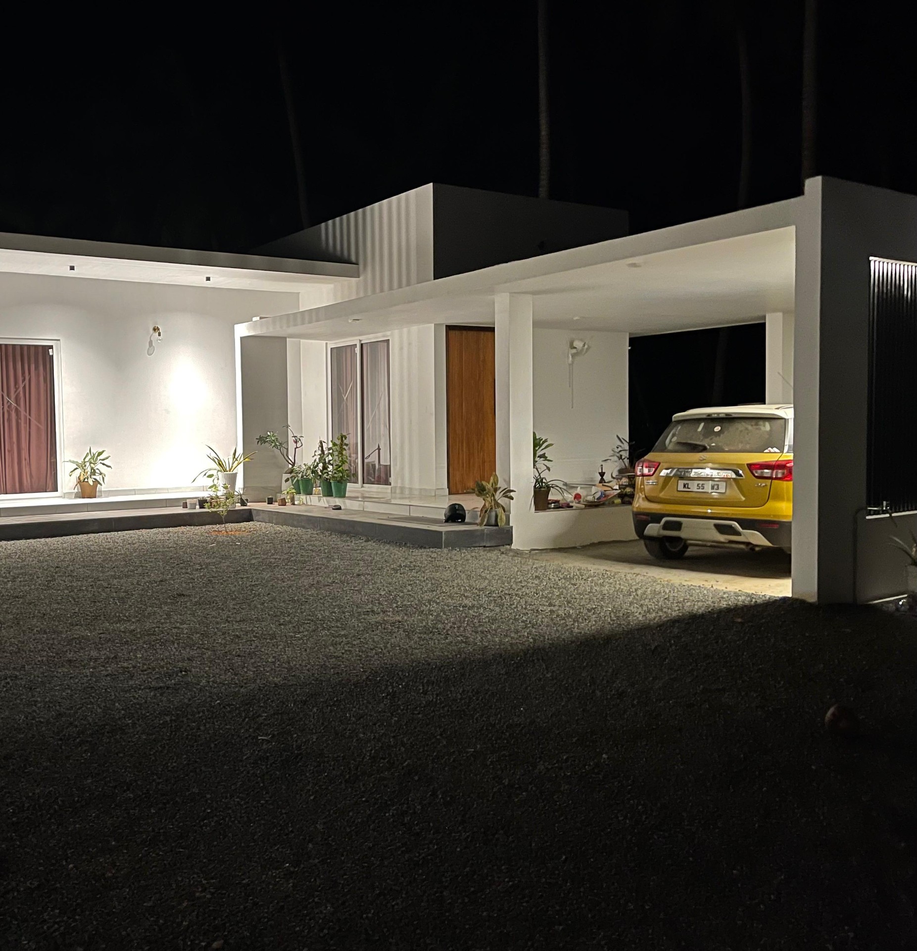 Night facade of a minimalist white flat-roof villa with illuminated carport designed by iptnirman